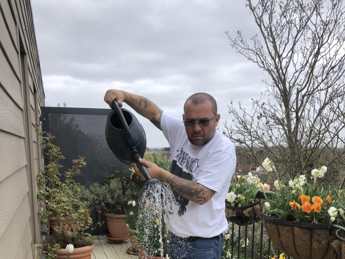 Chris Collins is watering various plant pots and trays of seeds on his balcony.